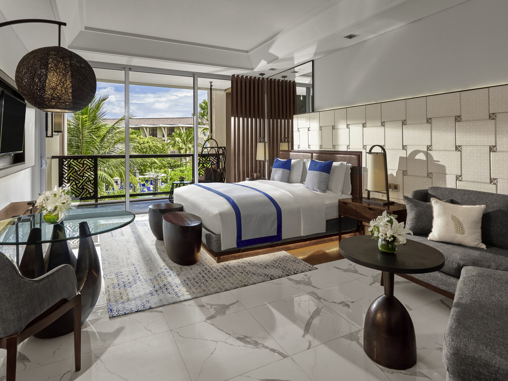 Chambre d'hôtel moderne avec lit, canapé et vue sur jardin tropical.